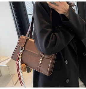 Close-up of brown vintage crossbody bag with metal rivets and plush ball charm detail
