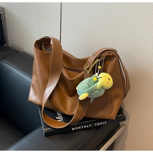 Detail view of brown leather tote with a green plush turtle charm and gold buckle accents