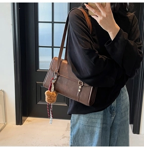 Detail view of a vintage dark brown leather shoulder bag with a plush bear charm on a model
