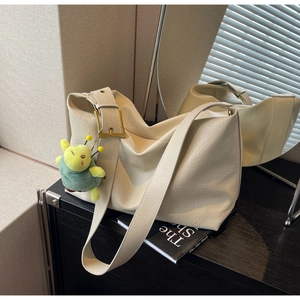 Detail of cream tote bag with large gold buckle and green plush caterpillar charm