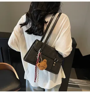 Detail of a black PU leather crossbody bag with a plush bear charm and plaid ribbon