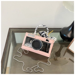 Detail of pink camera-shaped crossbody bag with silk scarf handle and metal chain strap