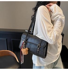 Detailed side view of black vintage messenger bag with bear charm and gold studs on model