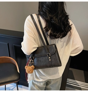 Detail of black leather square tote bag with cute brown bear charm and plaid ribbon