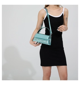 Detail of metallic teal crocodile pattern handbag worn with black dress in studio