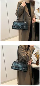 Detail of black glossy faux leather shoulder bag with vintage buckles worn on trench coat
