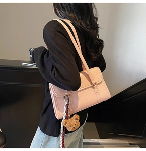 Close-up of pink leather crossbody bag with brown teddy bear charm and metal buckle
