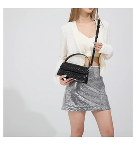 Detail of black crocodile texture handbag with adjustable strap on a fashion model
