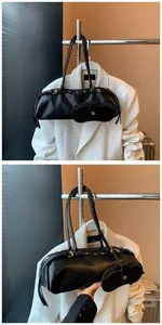 Detail of black leather baguette bag featuring slender handles and a detachable mini pouch