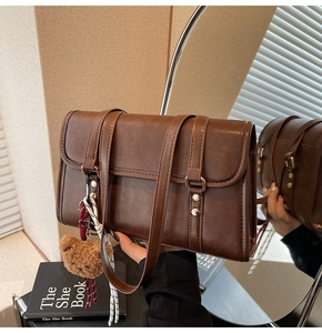 Detail of a brown leather shoulder bag featuring a cute teddy bear charm and metal buckles