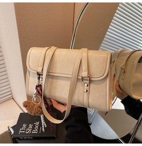 Close-up of cream beige crossbody bag with gold stud details and a plush bear charm