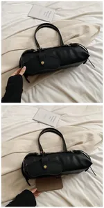 Detail of black leather baguette bag with gold hardware and mini charm attachment