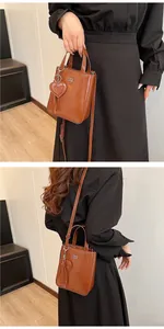 Detail view of brown glossy leather mini crossbody bag with heart charm and shoulder strap