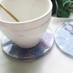 Detail of round resin coaster featuring embedded purple and blue dried flowers with cup