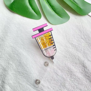 Macro shot of syringe-shaped acrylic badge with pink glitter and 'I CALL THE SHOTS' text