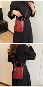 Detail of dark red oil wax leather mini tote bag with logo and heart charm on model