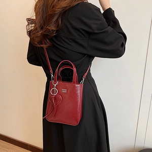 Burgundy patent leather mini tote bag with silver logo worn with black dress