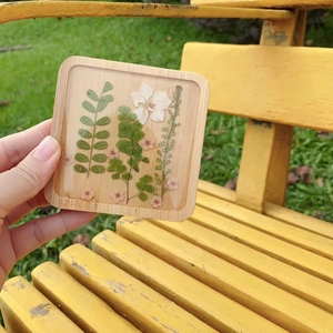 Detail of square wooden coaster with real pressed flowers and leaves in clear resin