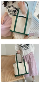 Detail of a large canvas tote bag featuring dark green trim and durable shoulder straps
