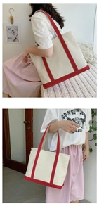 Detail of a large beige canvas tote bag with red handles shown on a model for daily style