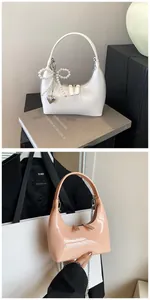 Détail du sac croissant en cuir verni brillant avec nœud perlé et breloque cœur