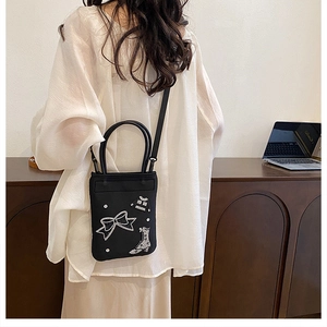 Detail of black fabric crossbody bag with white bow and boot embroidery motifs