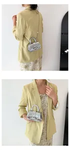 Close-up of model wearing mini silver laser handbag with elegant metal chain strap