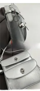 Detail of silver metallic textured crossbody bag with spherical charm and metal lock