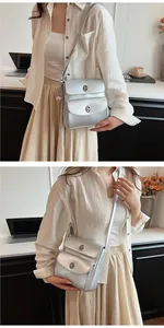 Detail view of silver metallic crossbody bag featuring round lock and ball charm accent