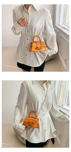 Detail of metallic orange mini square bag with handle and chain strap on white shirt