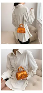 Detail of mini metallic orange bag with glossy finish and delicate silver chain strap