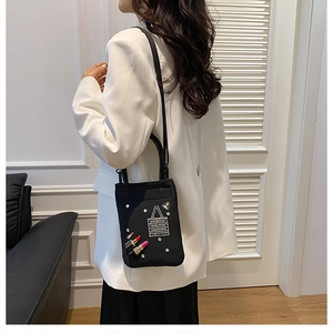 Detail of a black mini nylon bag featuring pearl accents and lipstick embroidery on white suit