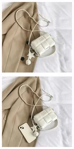 Detail of white woven crossbody bag with star charm and leather brand embossing