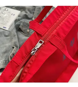 Gros plan sur le zip métallique argenté et la bandoulière en nylon rouge du sac