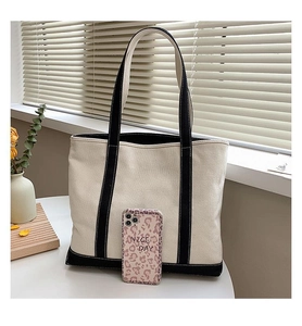 Detail of canvas tote bag with black handles next to a leopard print phone for scale