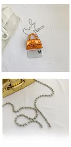 Macro detail of glossy orange mini bag with silver ball chain next to smartphone
