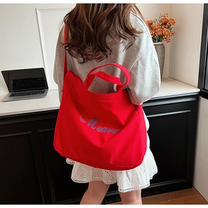Détail d'un sac cabas en toile rouge avec broderie Meare porté par un mannequin en intérieur