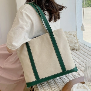 Minimalist canvas tote bag with green straps shown from a side-back view on a model