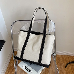 Minimalist canvas tote bag with black trim and long straps on a modern chair