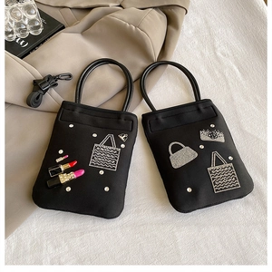 Detail of black mini handbag with rhinestone pattern and lipstick charm on white background