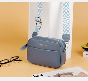 Detail of grey-blue leather crossbody camera bag with geometric wave pattern strap