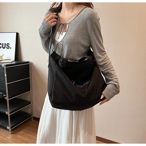 Gros plan du sac cabas en toile noire avec broderie cursive bleue et larges bandoulières