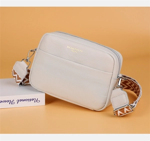 Detail of cream camera bag in lychee leather with gold logo and wide geometric strap
