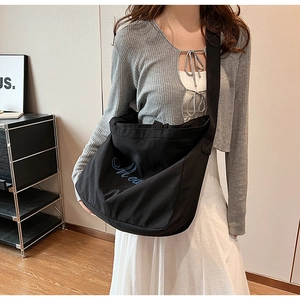 Gros plan sur un sac messager en toile noire avec broderie artistique bleue minimaliste