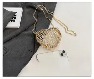 Detail of a gold heart-shaped hollow metal bag with mesh texture and fine chain strap