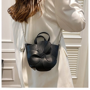 Detailed view of black floral petal handbag with silver chain strap on white blazer