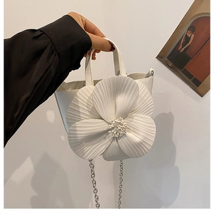 Detail of elegant white bucket bag featuring a large 3D flower with pearl center and chain