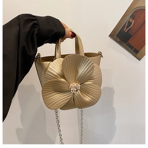 Close-up of golden bucket bag with 3D flower decoration and metallic chain strap
