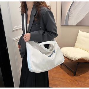 Gros plan d'un cabas en toile blanche avec texte bleu porté sur un blazer gris