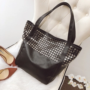 Black faux leather tote bag with silver studs on a white chair with high heels